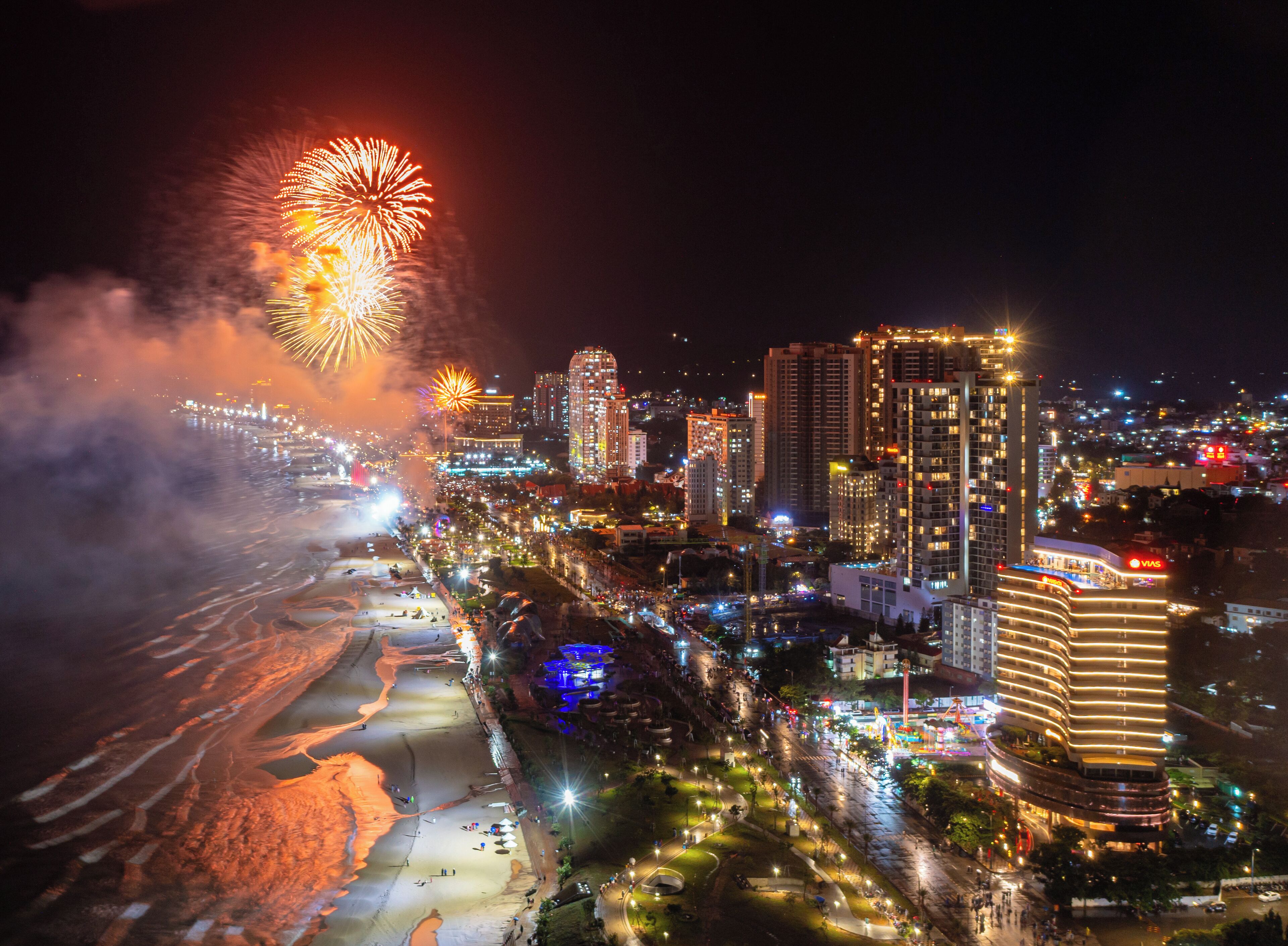 Un paysage urbain avec de hauts immeubles, une plage et des feux d’artifice.