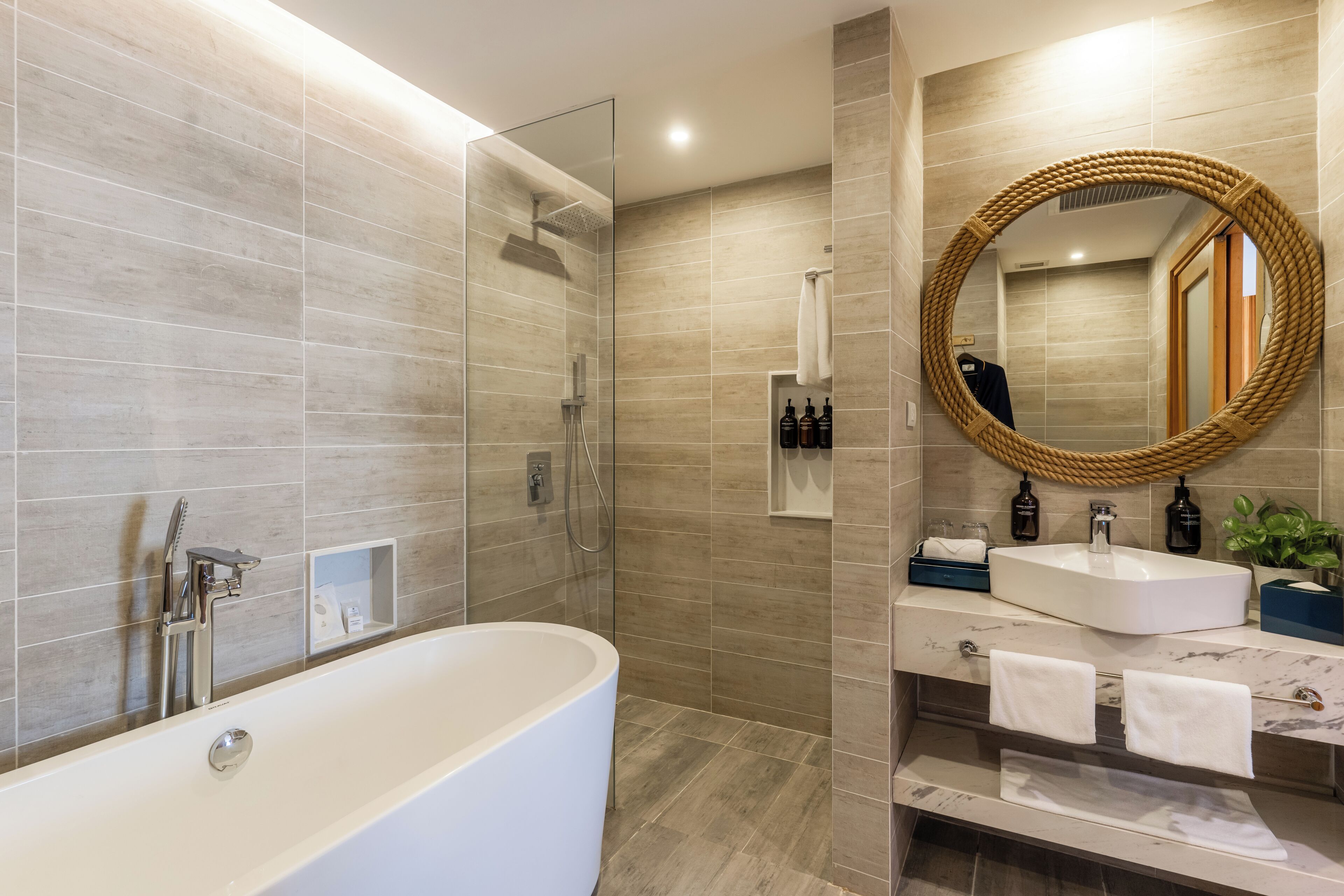 Une salle de bain moderne avec une baignoire sur pieds, un grand miroir doté d’un cadre tressé et un lavabo encastré avec un plan de travail en marbre.