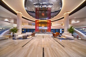 Un hall d’entrée spacieux avec un comptoir d’accueil central, des espaces de détente et un grand élément décoratif au plafond qui réfléchit la lumière.