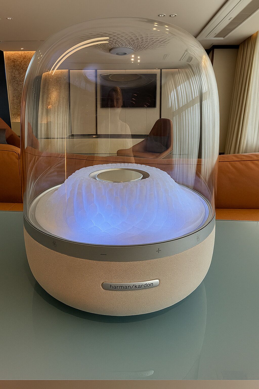 A modern, spherical, transparent enclosure with a light source inside, placed on a table in a room with a minimalist design, featuring a sofa and a framed picture on the wall.
