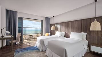A hotel room with two beds, a desk, a chair, a lamp, and a view of the ocean.
