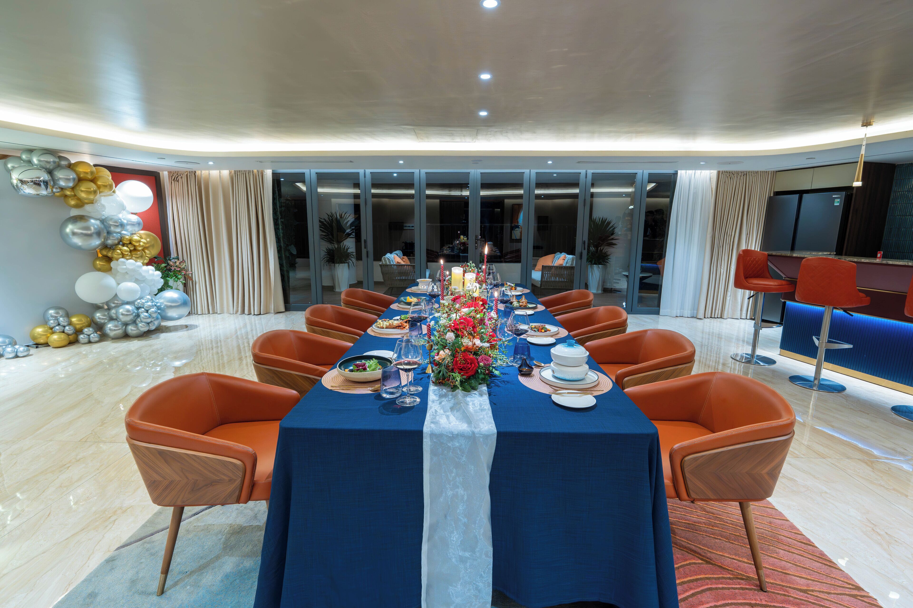 Una llarga taula de dinar preparada per a un àpat, amb caires taronja, un mantell blau i una peça central floral.