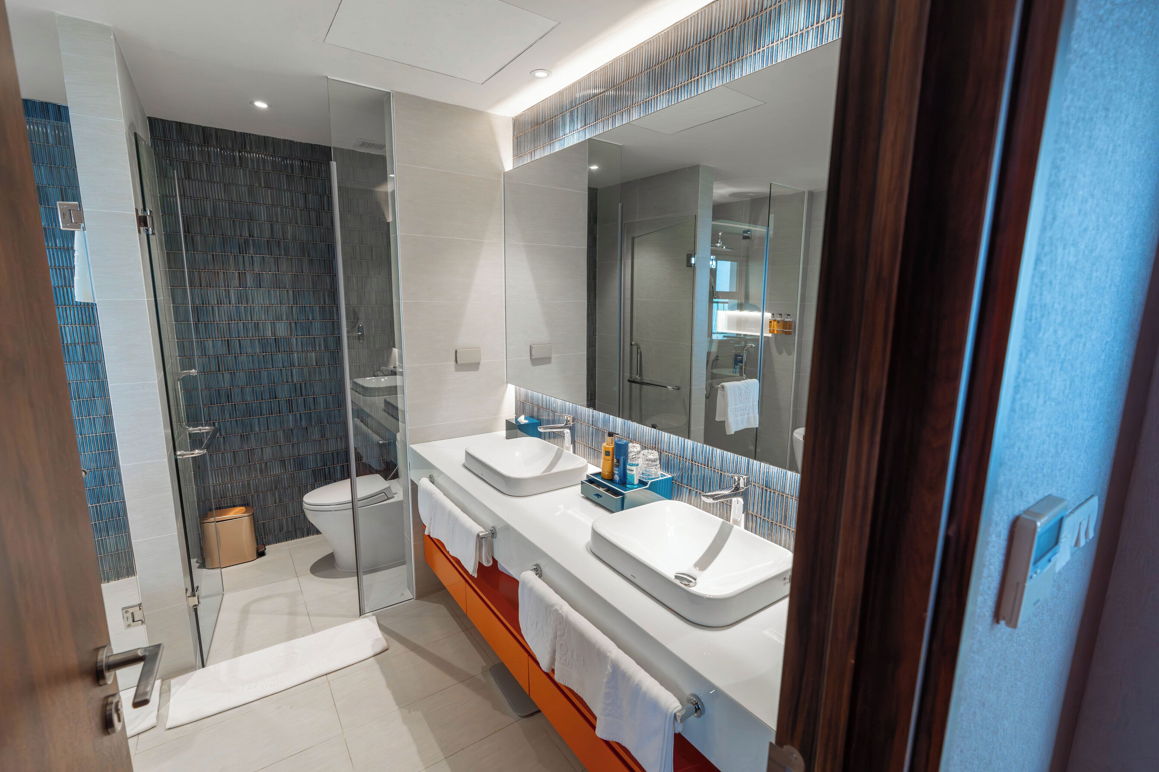 Een moderne badkamer met twee wasbakken, een douchecabine van glas en een grote spiegel.