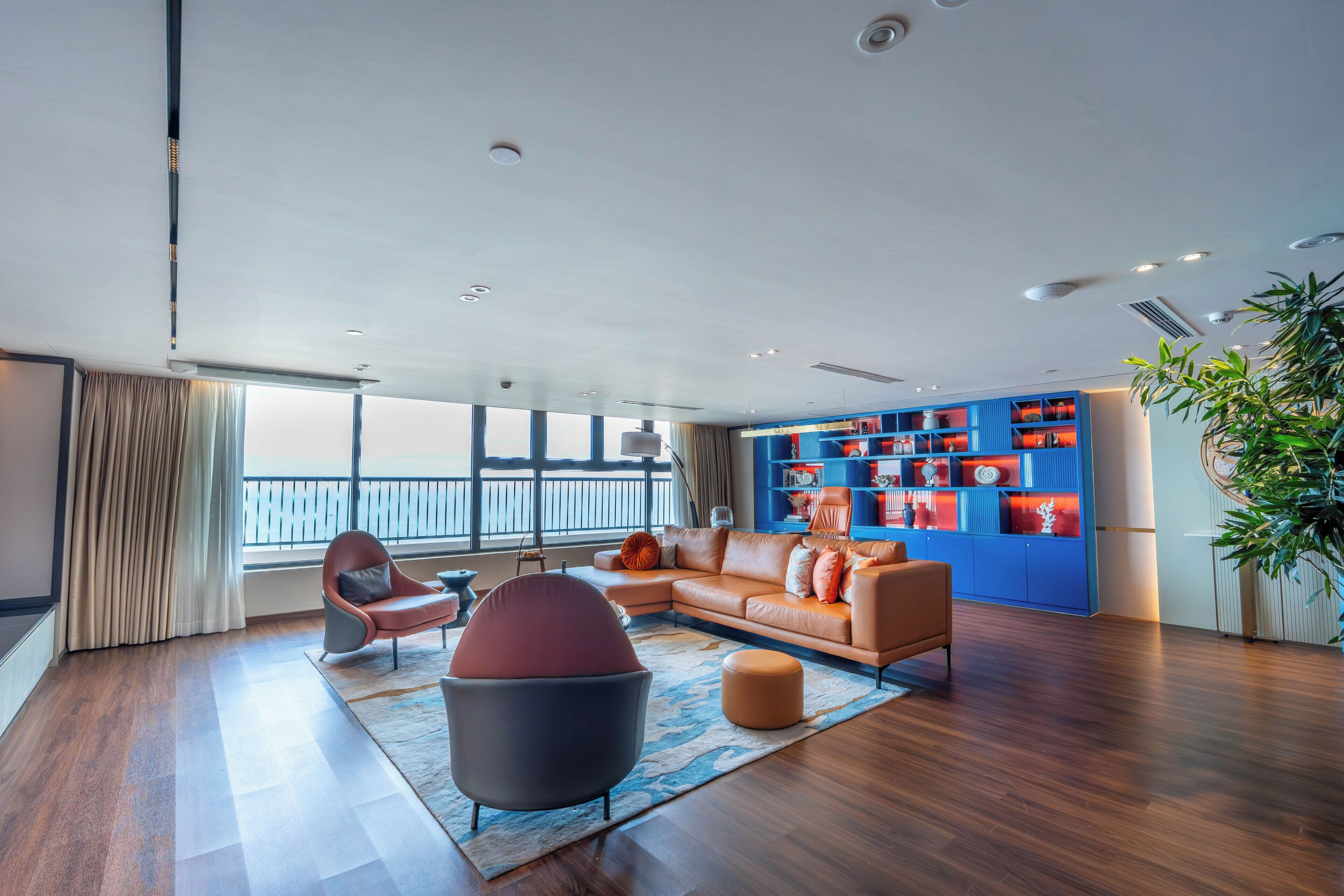 A modern living room with a leather sofa, a round ottoman, and a blue shelving unit against the wall.