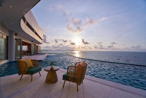 A poolside area with wicker chairs and a table, overlooking a large body of water and a modern building.