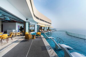 A rooftop infinity pool with lounge chairs and umbrellas, overlooking a body of water.