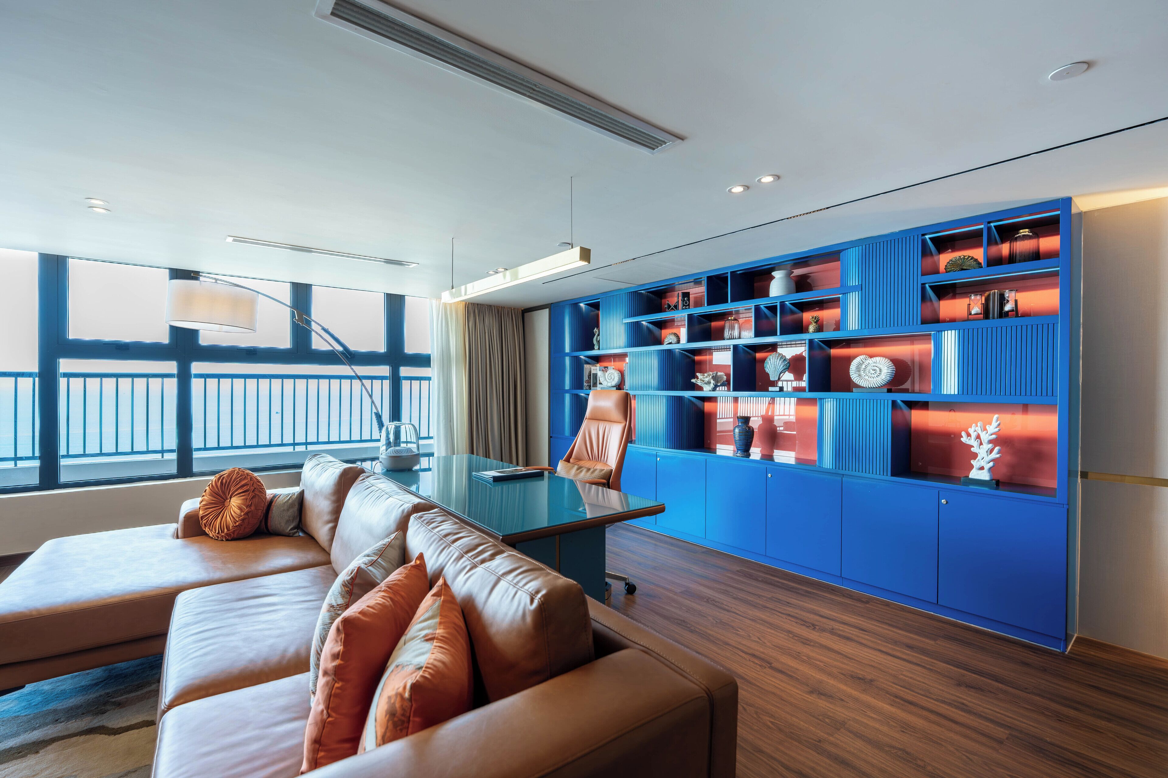 A modern living room with a leather sofa, a glass coffee table, and a blue shelving unit with decorative items.