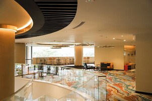 Un hall d’entrée spacieux doté d’une rambarde en verre, d’un sol en marbre et d’un espace détente avec des chaises et des tables.