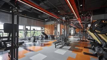 Ein Fitnessstudio mit verschiedenen Trainingsgeräten, großen Fenstern und einem Schachbrettmuster auf dem Boden.