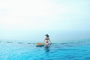 A person in a bikini standing in a clear blue pool with a basket of fruit.