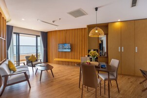 A modern hotel room with a dining area, a television mounted on a wooden panel wall, and a balcony with a view.