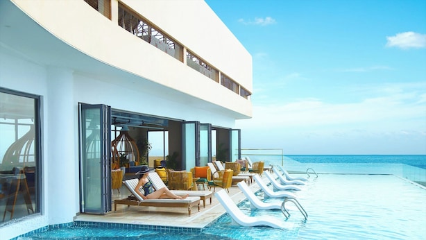 A poolside area with lounge chairs and a glass-enclosed balcony overlooking the ocean. - Vias Hotel Vung Tau (Ho Chi Minh City)