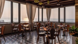 A restaurant with tables and chairs arranged for dining, large windows with curtains, and a view of the sea. - Vias Hotel Vung Tau (Ho Chi Minh City)