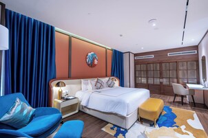 A modern hotel room with a large bed, a desk, a chair, and a sofa.