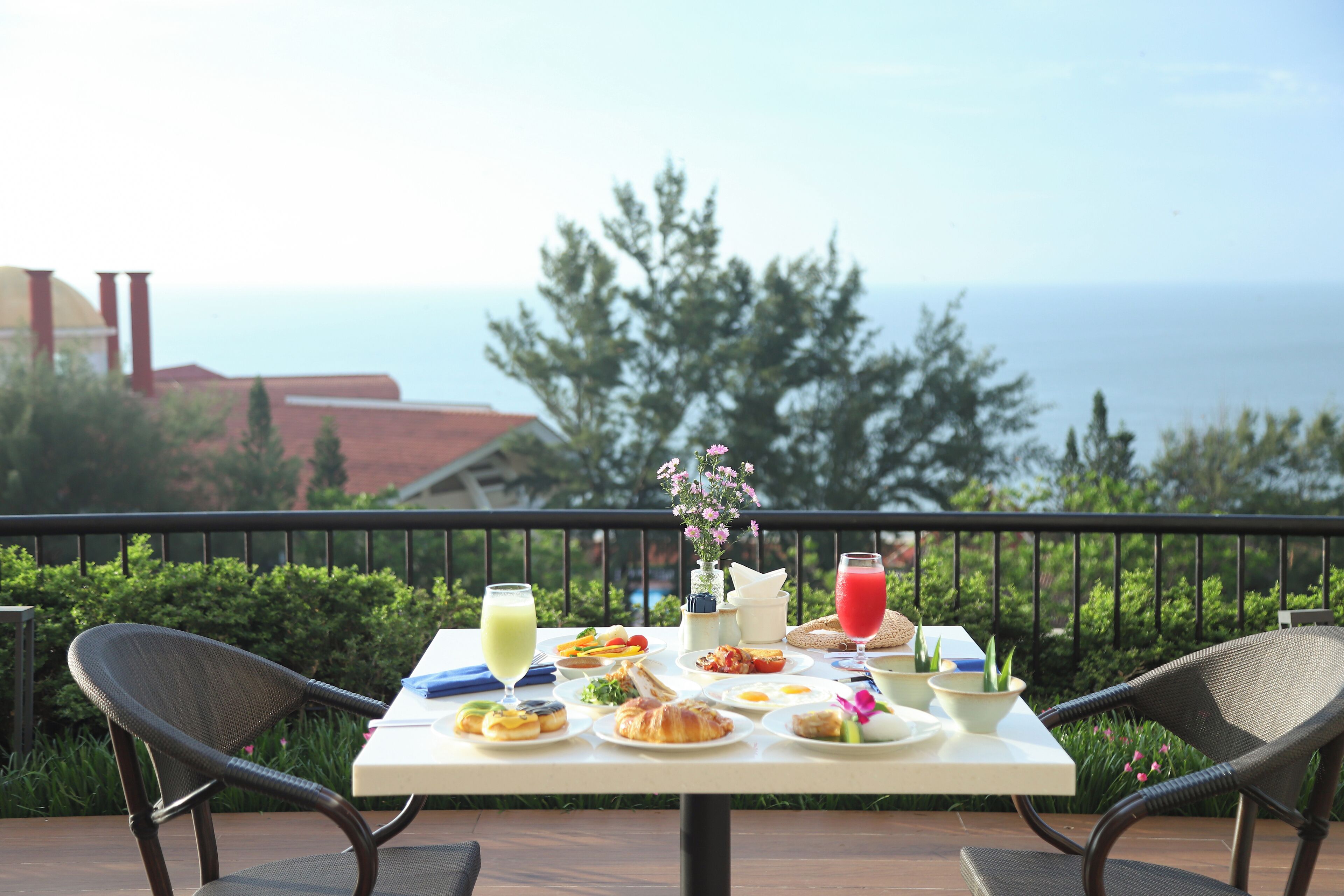 A table set with breakfast items and drinks on a balcony overlooking the sea.