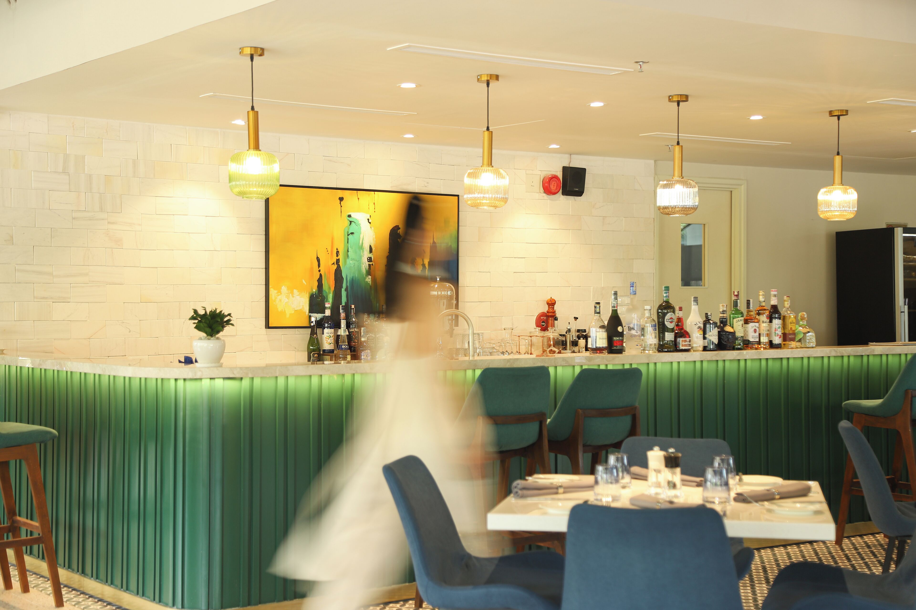 A bar area with a green counter, multiple hanging lights, and a large painting on the wall.