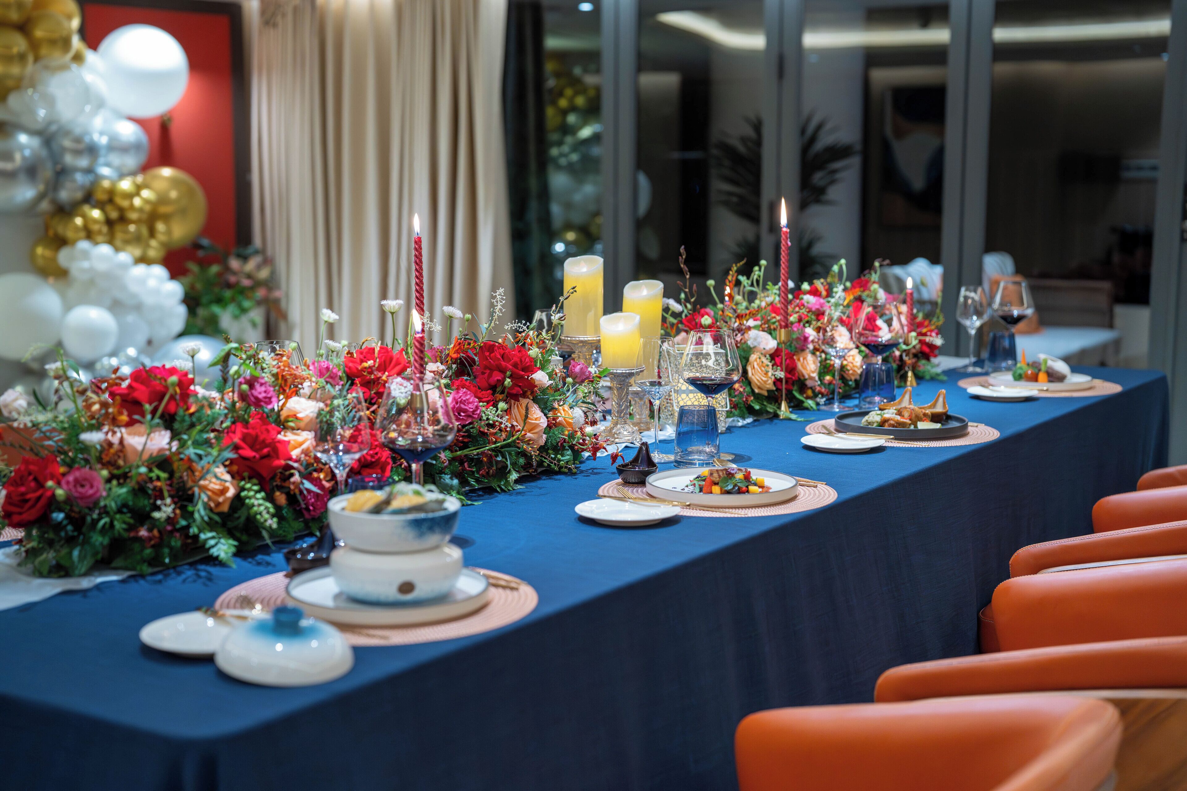 Una larga mesa de comedor dispuesta con platos, vasos y velas, rodeada de sillas naranjas.