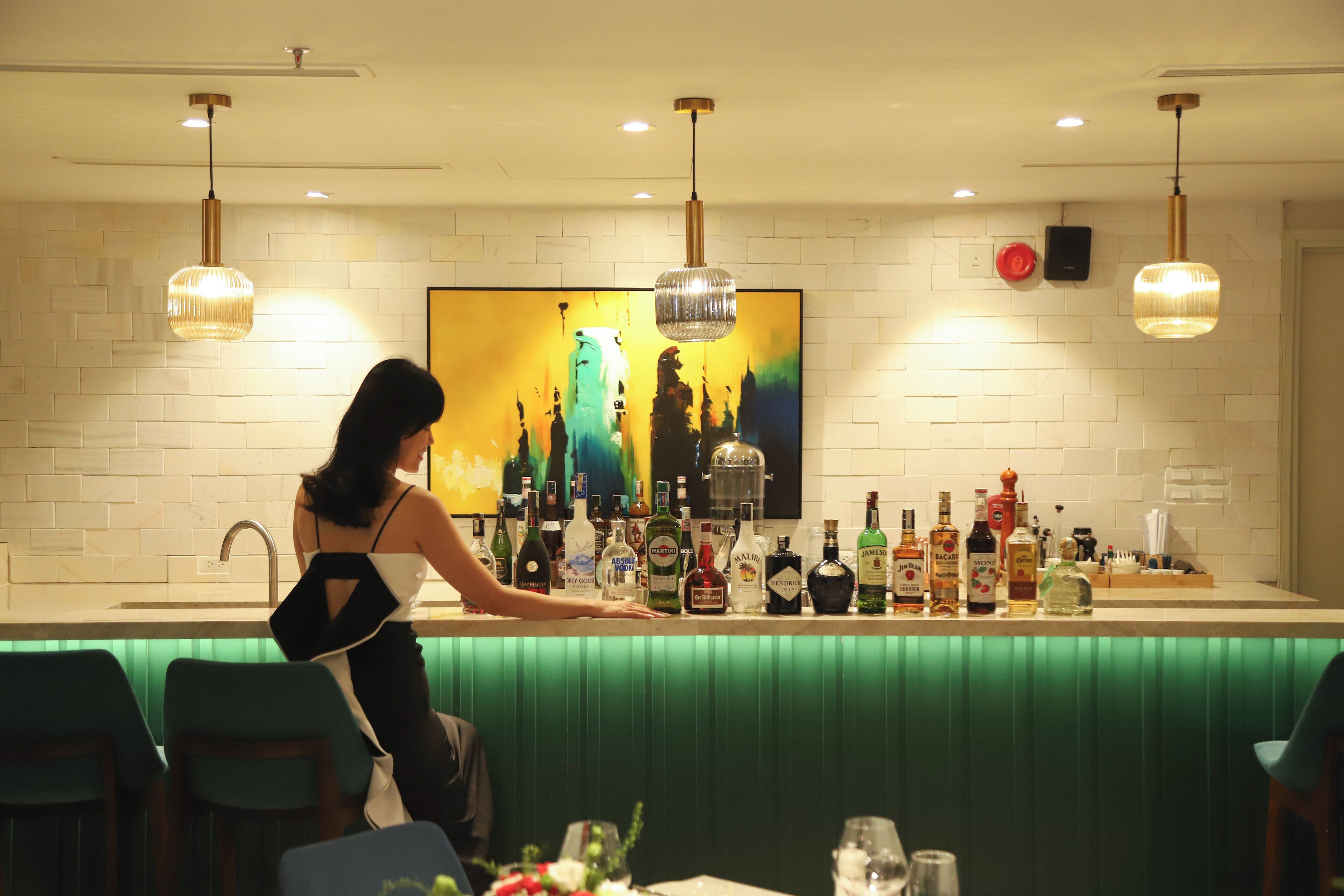Zona de bar con un cantinero, una variedad de botellas de licor y un cuadro grande en la pared.