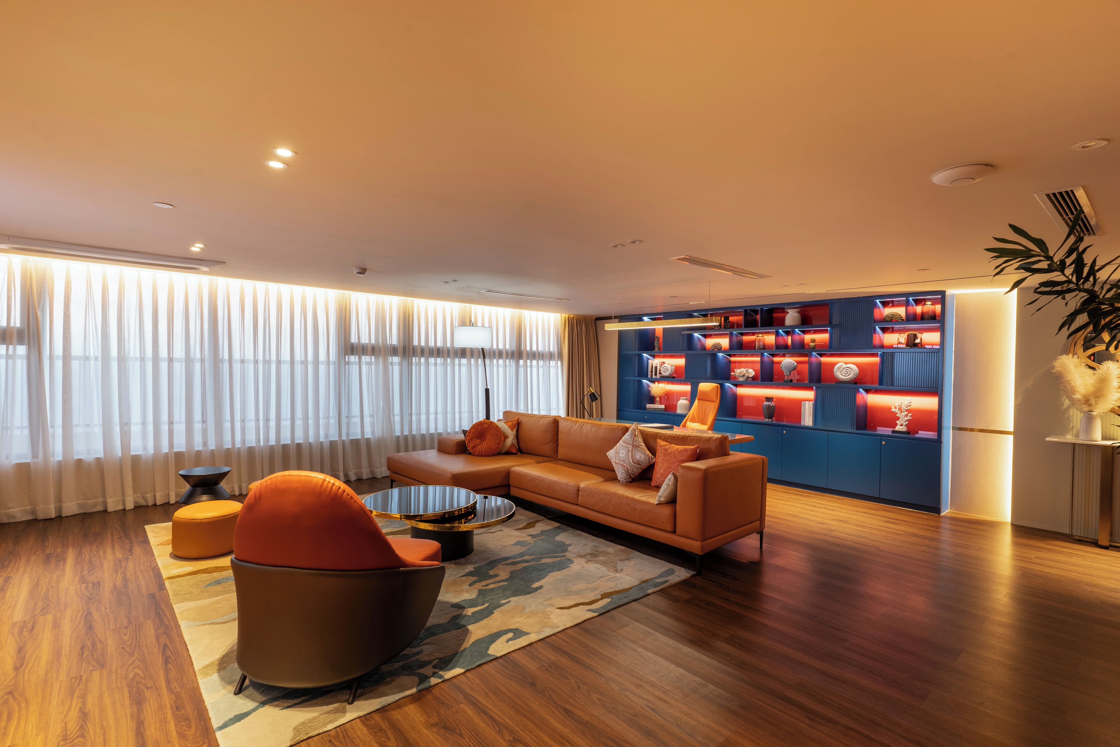 A modern living room with a sectional sofa, a round coffee table, and a vibrant red accent wall with shelves.