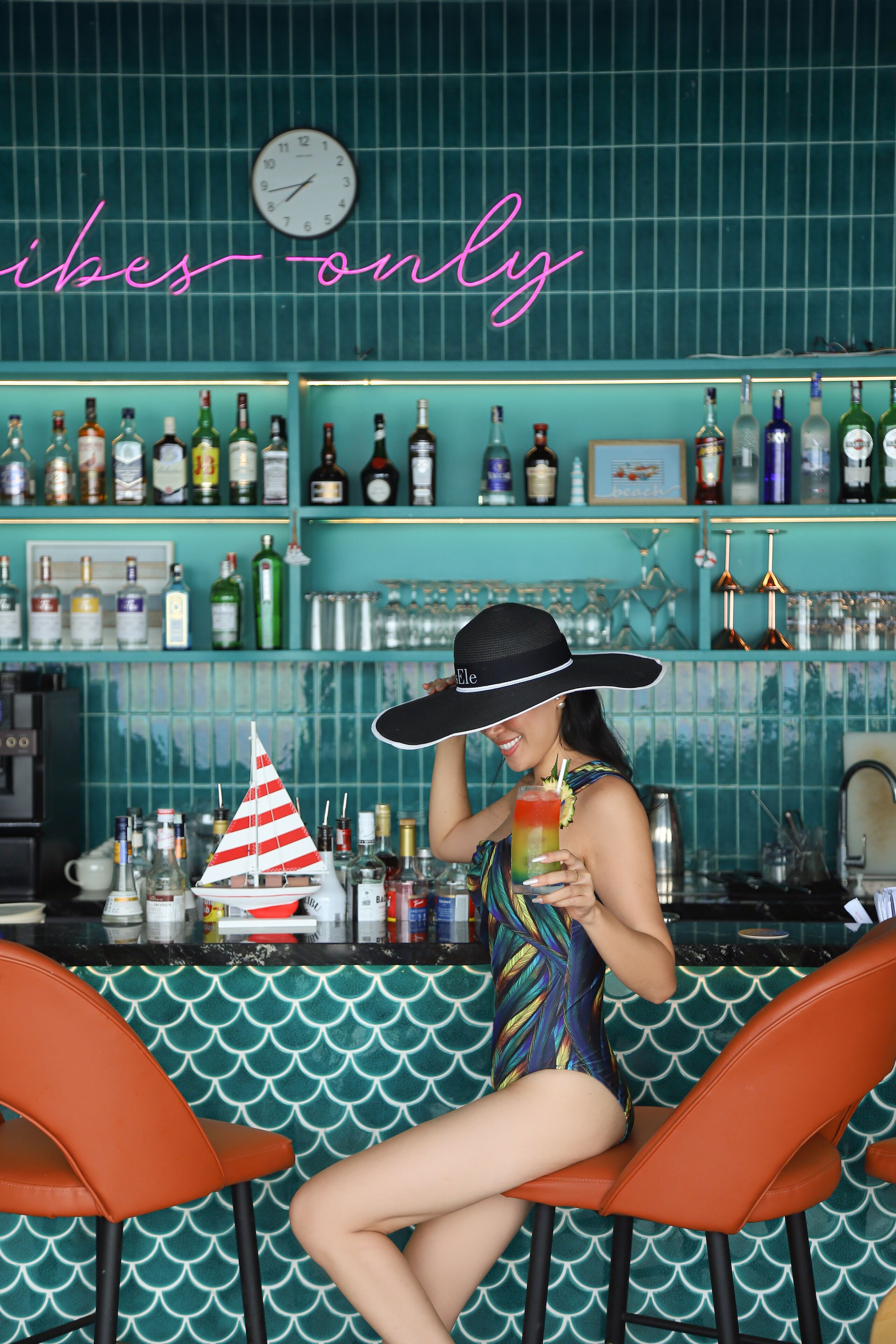 A bar area with a neon sign, various bottles, and two orange chairs.