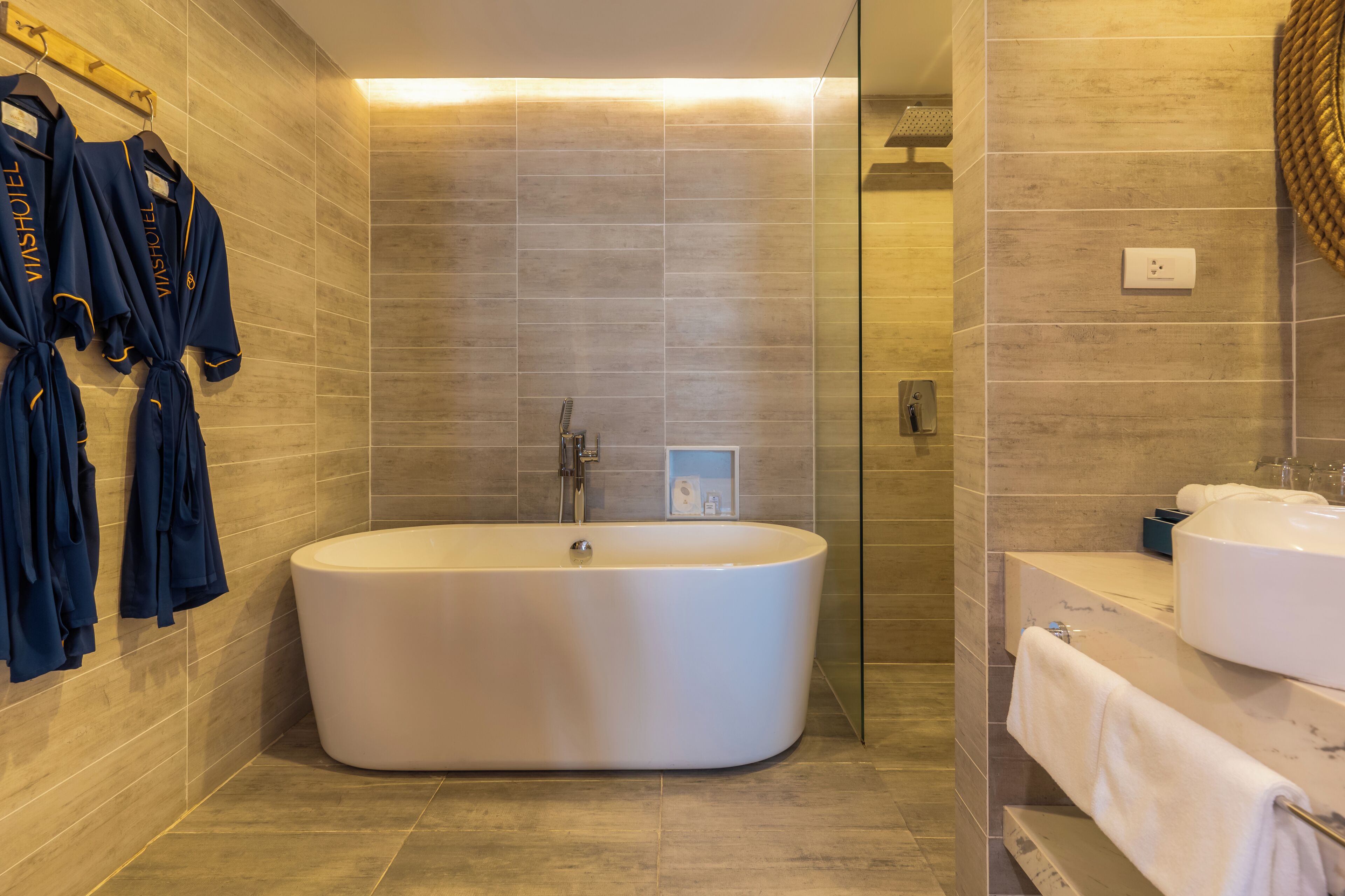 Un baño moderno con una bañera independiente, cabina de ducha con mampara de vidrio y tocador con lavabo y toallero.
