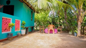A turquoise building with pink decorative panels, a covered outdoor seating area with chairs, and potted plants. - Nilaveli Beach Inn (Nilaveli)