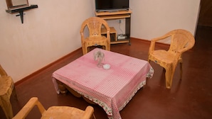 A small room with a table covered by a checkered tablecloth, two wooden chairs, a television on a stand, and a wall-mounted shelf. - Nilaveli Beach Inn (Nilaveli)