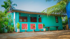 A turquoise house with three windows, a door, and a small porch area with potted plants. - Nilaveli Beach Inn (Nilaveli)