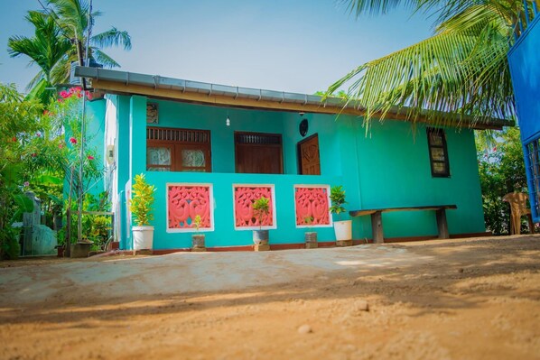 A turquoise house with three windows, a door, and a small porch area with potted plants. - Nilaveli Beach Inn (Nilaveli)