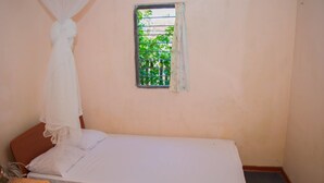 A single bed with a white canopy, a small window with a metal grill, and a plain wall. - Nilaveli Beach Inn (Nilaveli)