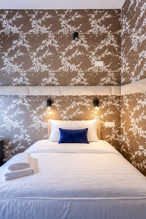 A neatly made bed with white and blue pillows, a folded towel, and two wall-mounted lights. - Amber Suite Szczecin Adults Only (Szczecin)