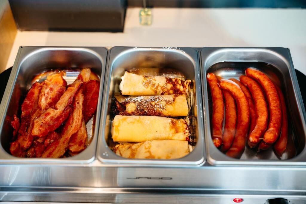 A buffet with three trays containing bacon, pancakes, and sausages.
