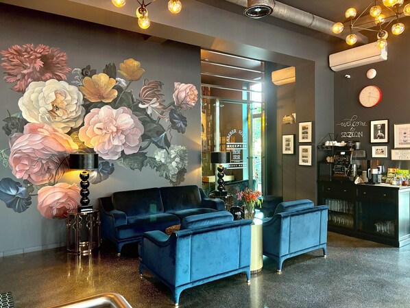Uma área de recepção com um sofá azul, um espaço para café e um mural de flores na parede.