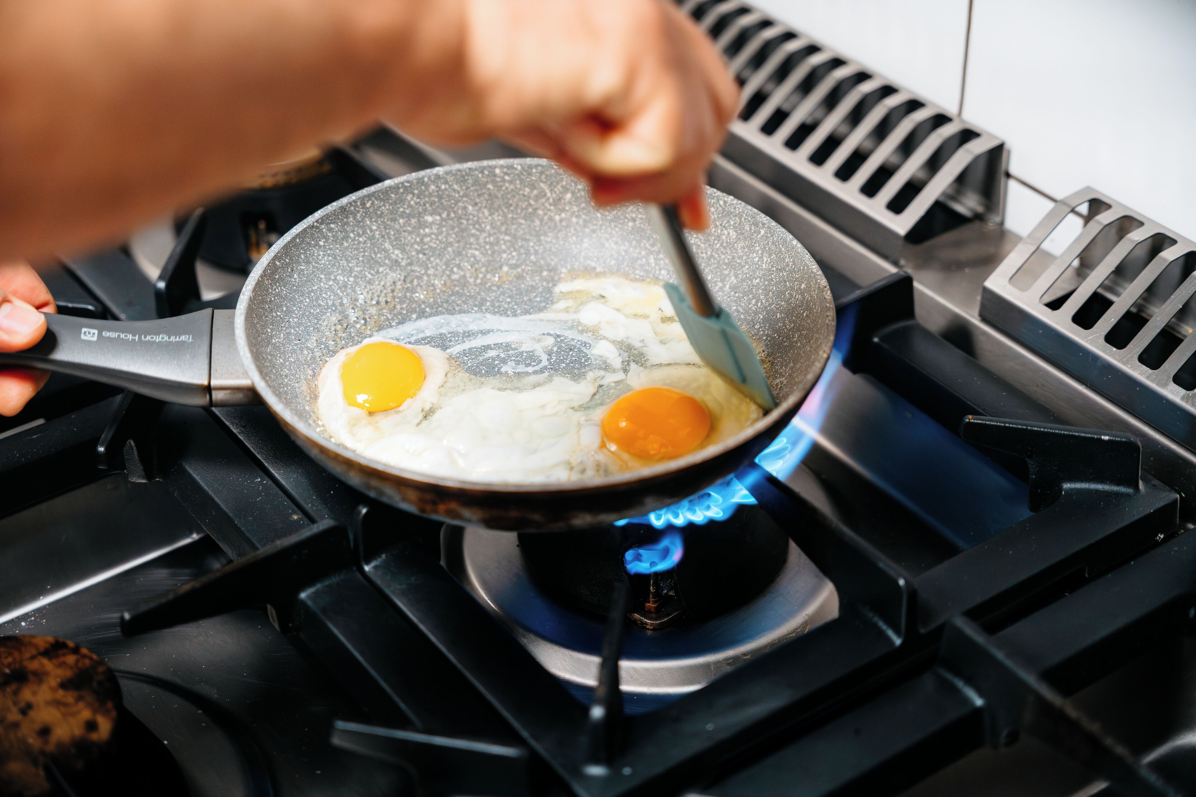 A hand cooking two eggs in a frying pan on a gas stove.