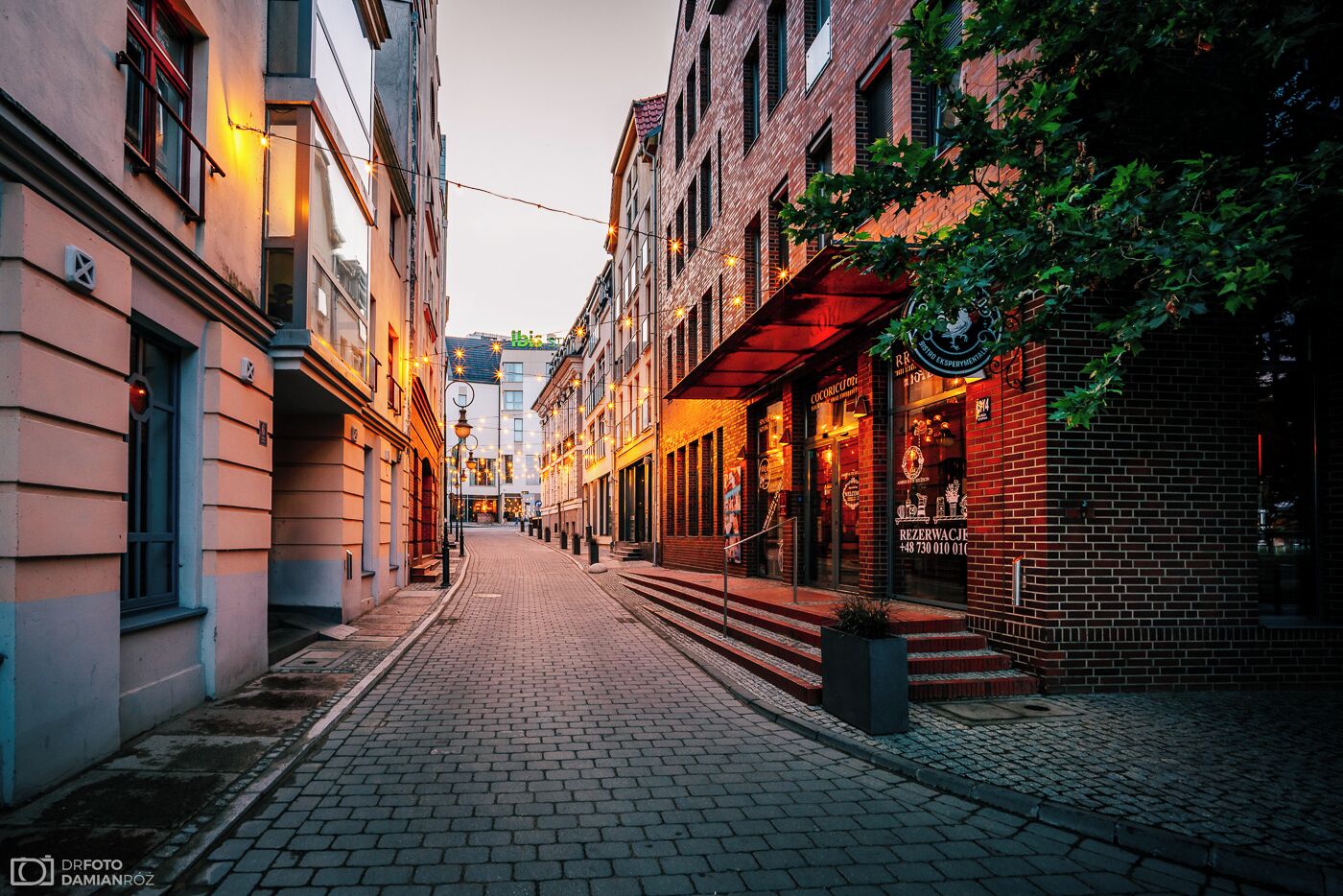 A narrow cobblestone street lined with buildings, some with visible signage and storefronts.