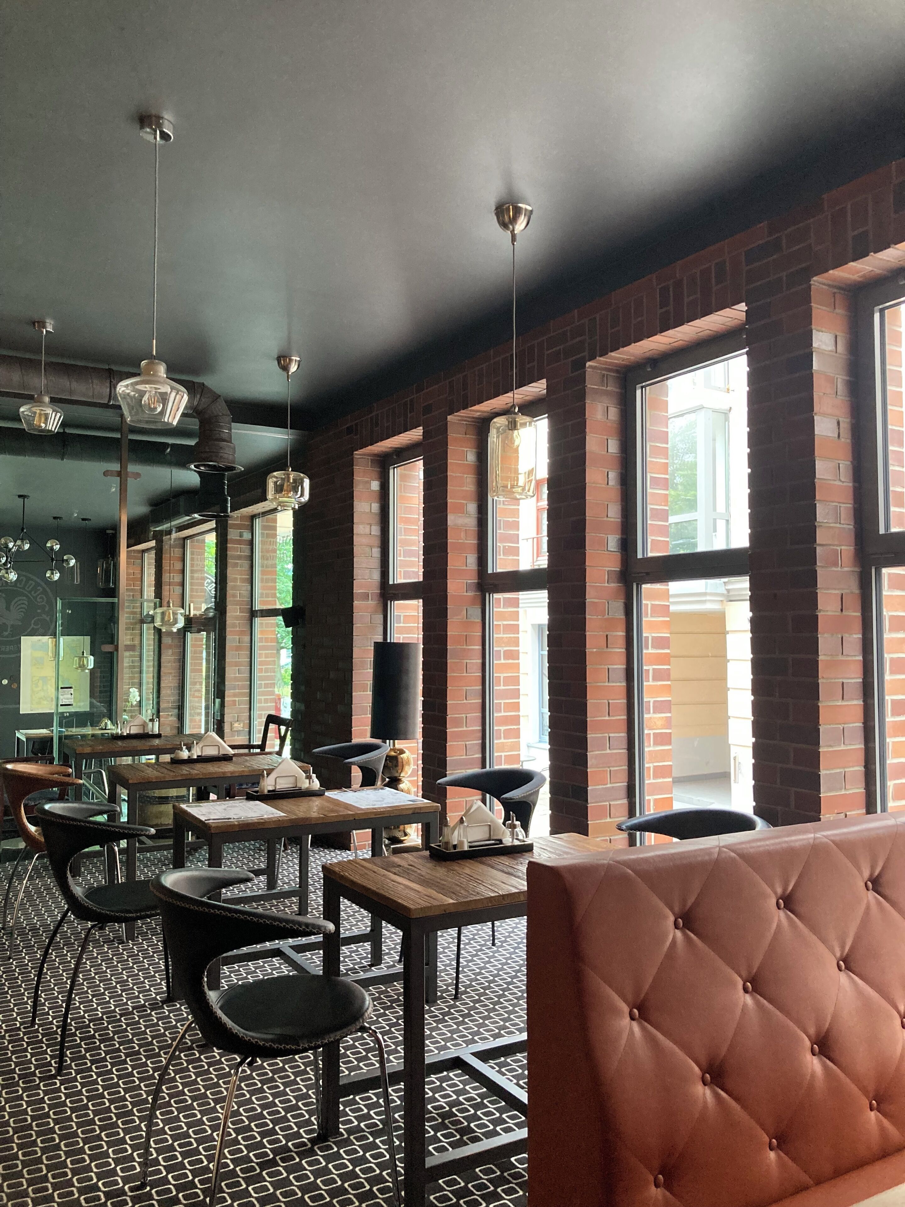 Interior de un restaurante con paredes de ladrillo, ventanas amplias y una combinación de mobiliario metálico y de madera.