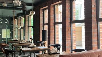 Interior de un restaurante con paredes de ladrillo, ventanas amplias y una combinación de mobiliario metálico y de madera.