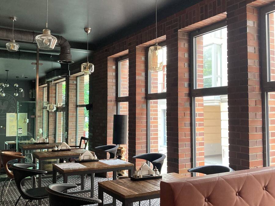 Interior de un restaurante con paredes de ladrillo, ventanas amplias y una combinación de mobiliario metálico y de madera.
