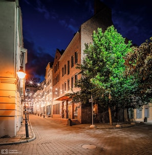 Una calle iluminada de noche con edificios, un árbol y un farol.