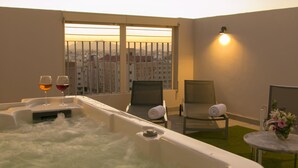 Una bañera de hidromasaje con dos copas de vino, una toalla y una silla en un cuarto con vista a edificios.