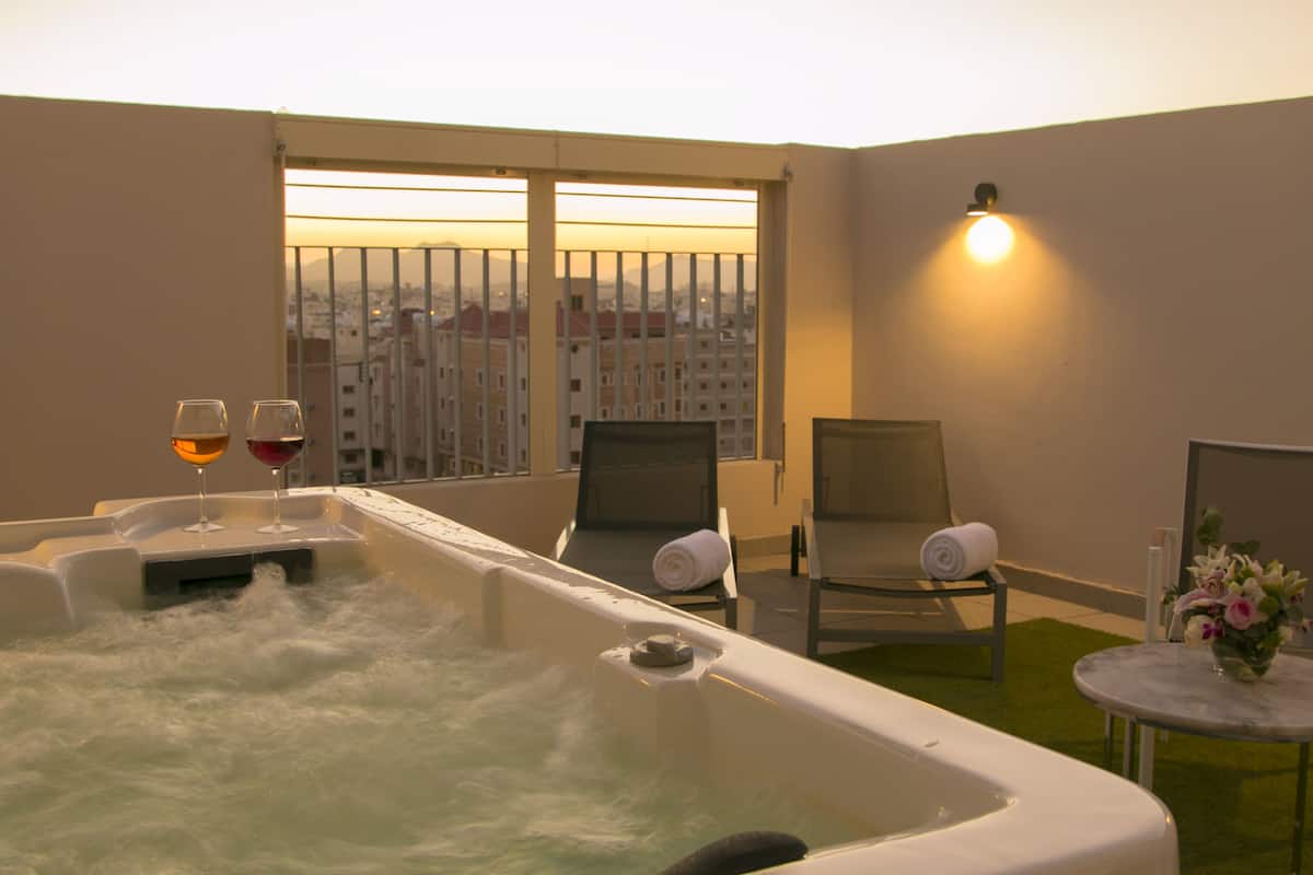 A hot tub with two glasses of wine, a towel, and a chair in a room with a view of buildings.