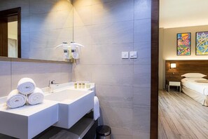A modern bathroom with a large mirror, white sink, and neatly rolled towels.