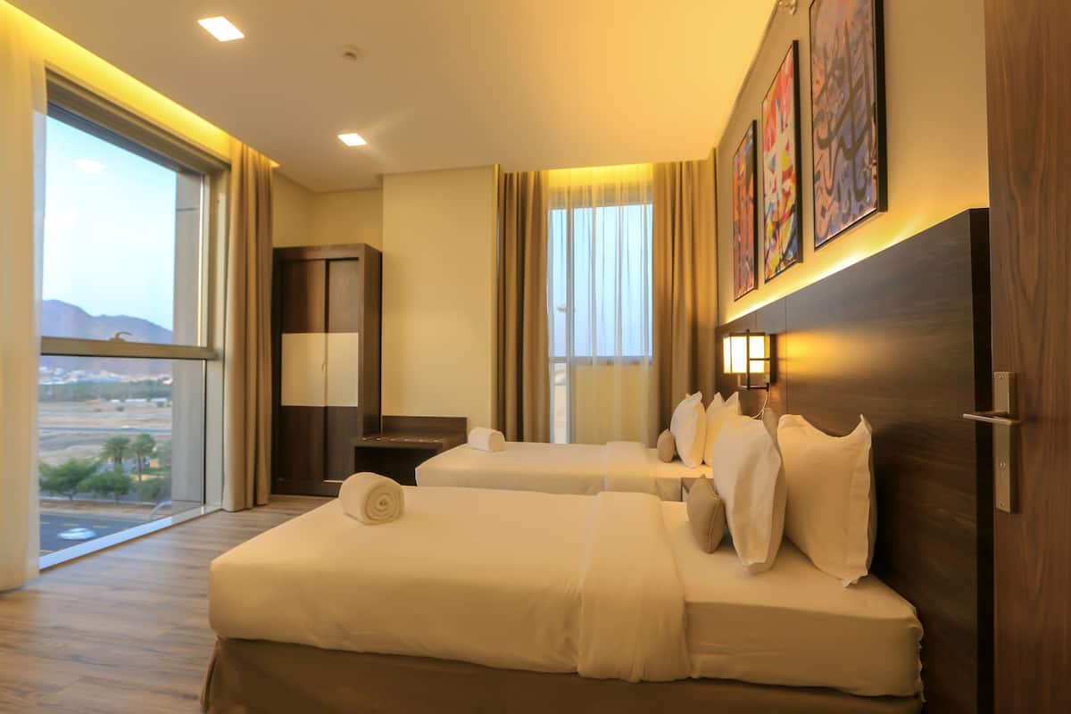 A hotel room with two beds, a desk, and a large window offering a view of the landscape.