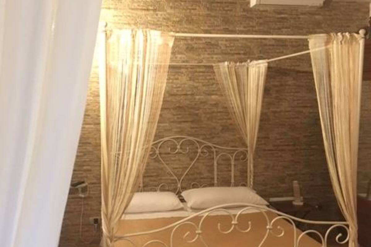 Ein Bett mit Baldachin, mit Metallgestell und weißer Bettwäsche, vor einer Steinwand mit Holzbalkendecke.
