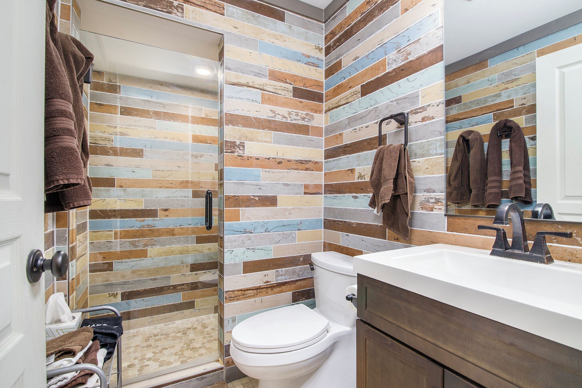 Un baño de diseño moderno, con inodoro blanco, lavabo con grifo oscuro y zona de ducha con puerta de cristal.