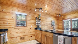 A wooden cabin kitchen with a central island, wooden cabinets, a built-in oven, and a window overlooking the forest.