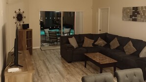 A spacious living room with a dark-colored sectional sofa, a wooden coffee table, and a dining area with a wooden table and chairs. - Free pool heat June, July, August Keyvilla-The Disney Retreat, 5 bed pool home.  (davenport)