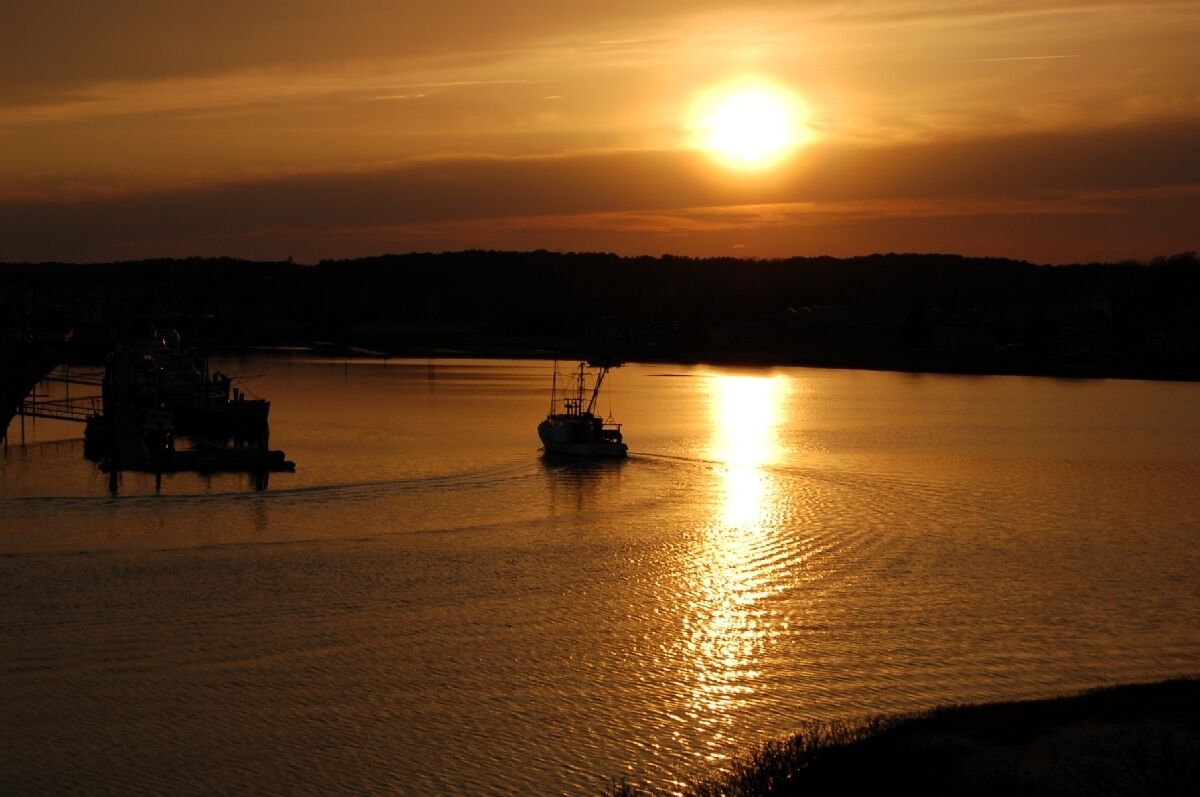 A sunset over a calm body of water with two boats.