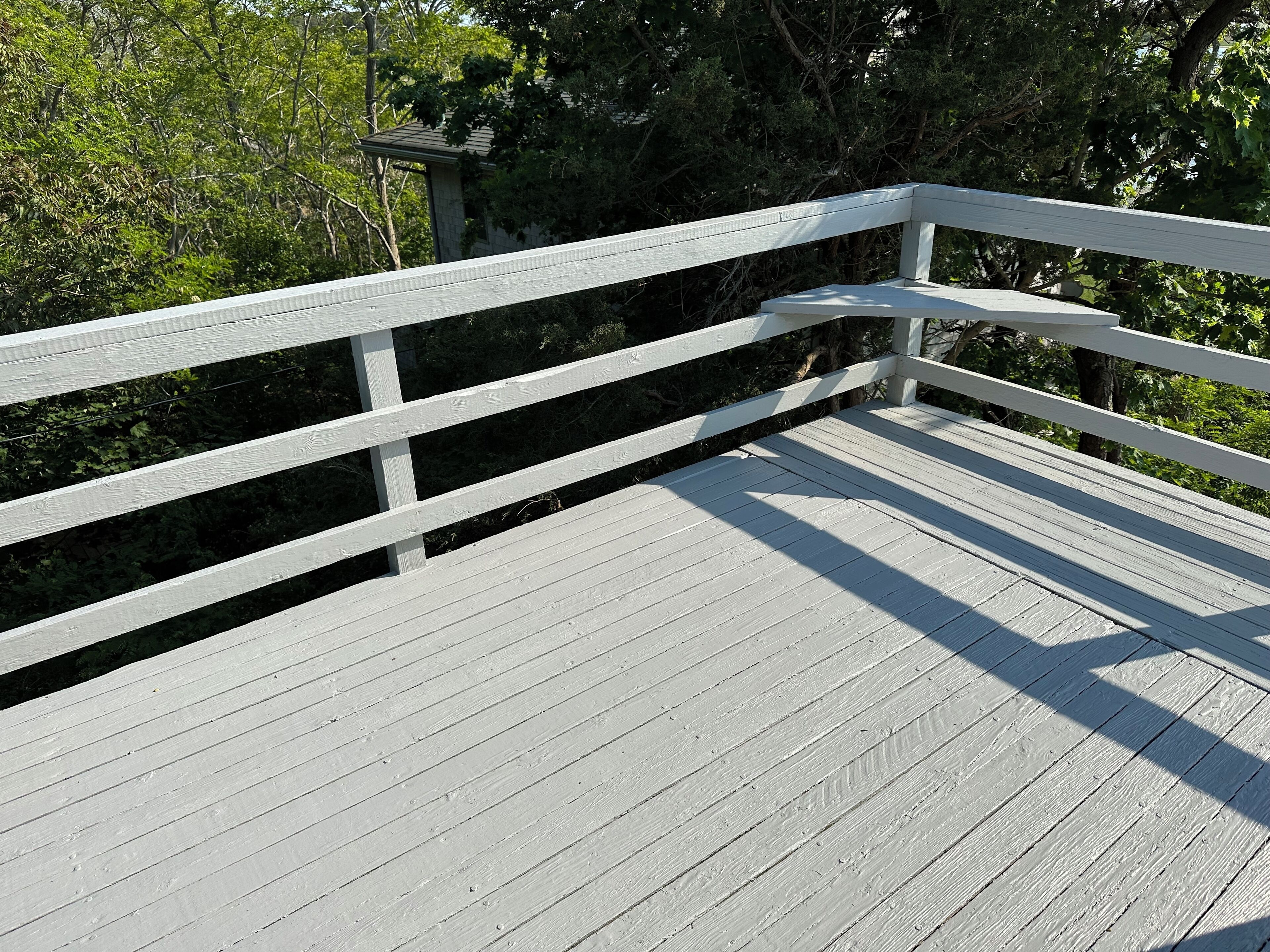 A wooden deck with white railings, surrounded by trees.
