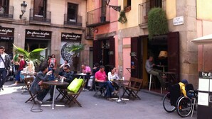 Un espace de café en plein air, avec des tables et des chaises, entouré d’immeubles dotés de balcons et de fenêtres.